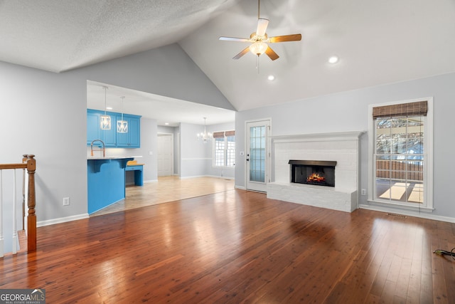 unfurnished living room with ceiling fan with notable chandelier, a sink, wood-type flooring, baseboards, and a brick fireplace