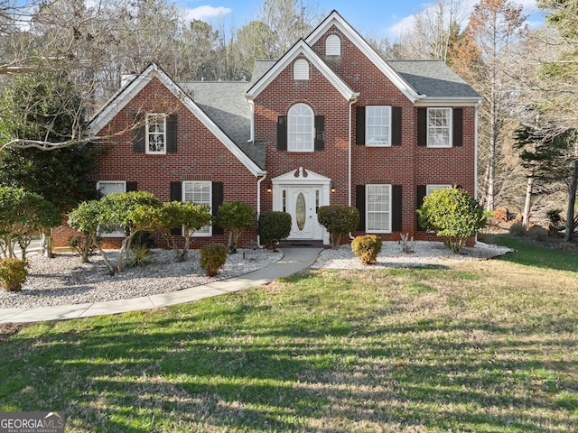 colonial-style house featuring brick siding, roof with shingles, and a front lawn