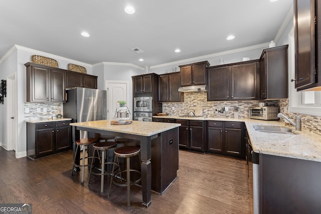 kitchen featuring under cabinet range hood, a sink, a kitchen island, appliances with stainless steel finishes, and dark brown cabinets