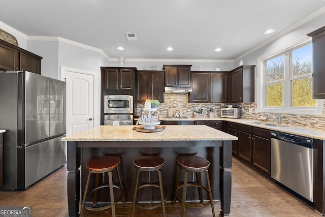 kitchen with visible vents, a sink, under cabinet range hood, appliances with stainless steel finishes, and a center island