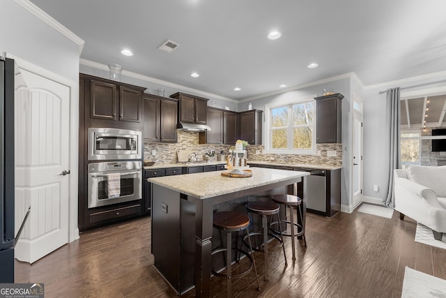 kitchen featuring visible vents, dark wood finished floors, stainless steel appliances, dark brown cabinetry, and under cabinet range hood