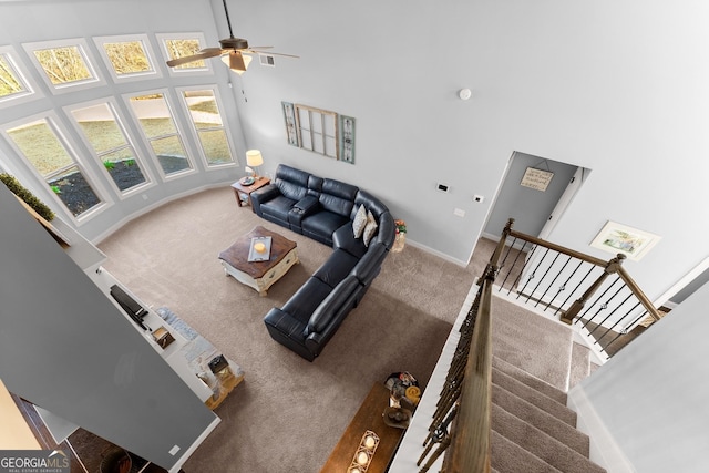 living area with ceiling fan, baseboards, carpet floors, and a towering ceiling