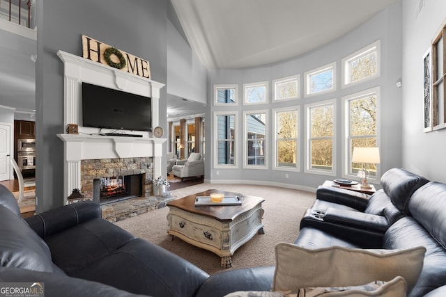 carpeted living room featuring baseboards, high vaulted ceiling, and a stone fireplace