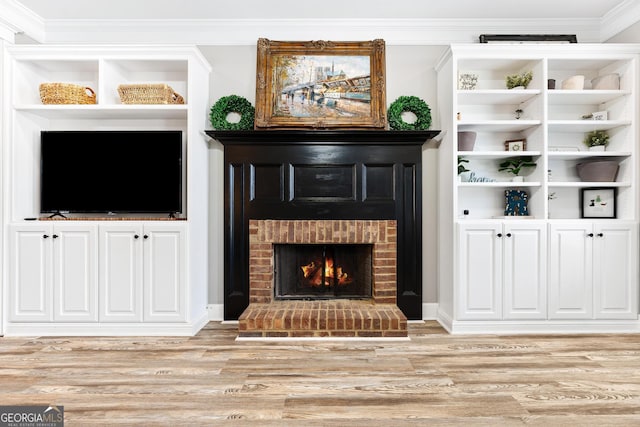 living area with a brick fireplace, built in shelves, light wood-style floors, and ornamental molding