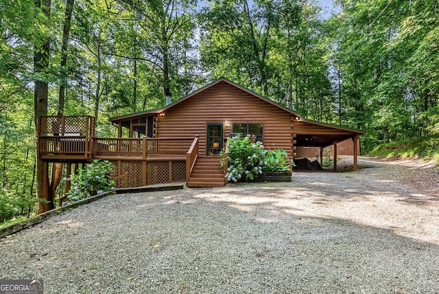 back of house featuring log siding, an attached carport, a deck, and driveway