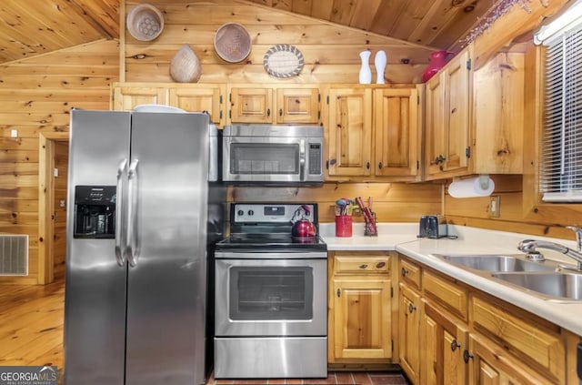 kitchen featuring vaulted ceiling, wood walls, appliances with stainless steel finishes, and a sink