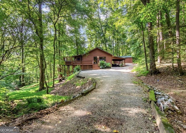 view of side of property with gravel driveway, a carport, a forest view, and a wooden deck