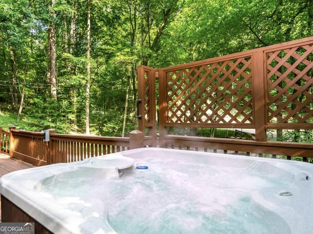 wooden terrace featuring a forest view and a hot tub