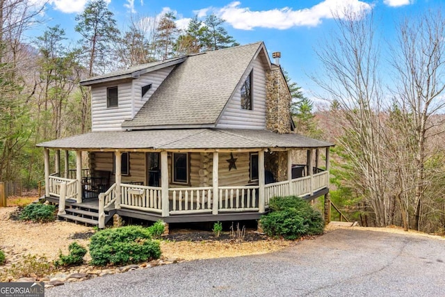 view of front of property featuring covered porch, a chimney, and a shingled roof