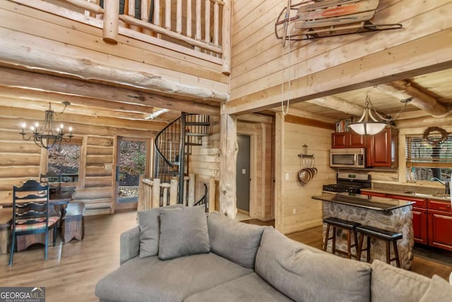 living room featuring a chandelier, beamed ceiling, stairs, rustic walls, and dark wood-style floors