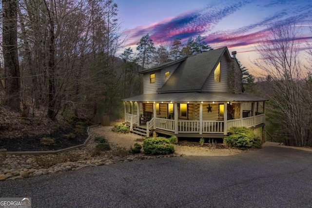 country-style home with driveway, covered porch, a chimney, and a shingled roof