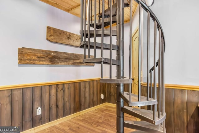 staircase with wood finished floors, wood ceiling, wood walls, and wainscoting