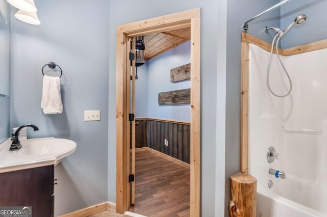 full bath featuring wooden walls, wood ceiling, wainscoting, wood finished floors, and washtub / shower combination