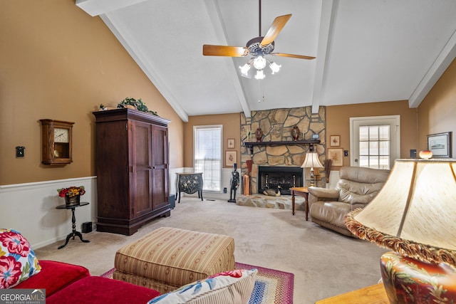 living room with vaulted ceiling with beams, a fireplace, ceiling fan, wainscoting, and light carpet