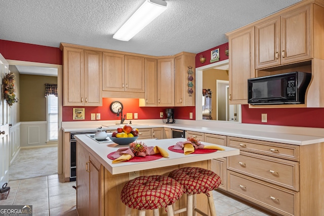 kitchen featuring a sink, light brown cabinetry, light countertops, black microwave, and wainscoting