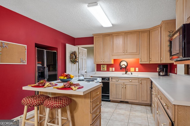 kitchen with a center island, black microwave, a kitchen bar, light countertops, and a sink