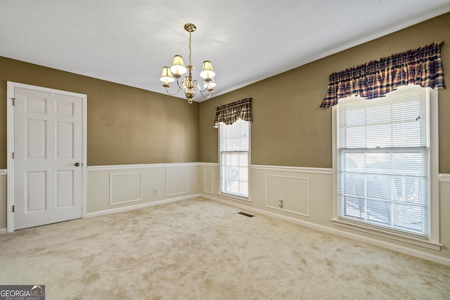 unfurnished room with a wainscoted wall, visible vents, carpet floors, a textured ceiling, and a chandelier