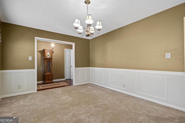 spare room with a decorative wall, a notable chandelier, carpet floors, and wainscoting