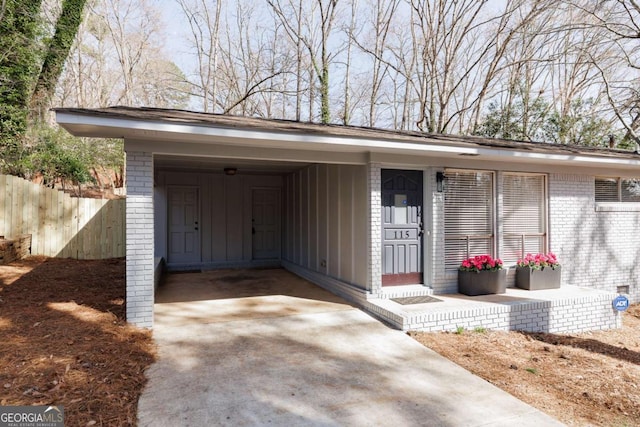 doorway to property with brick siding, concrete driveway, and fence