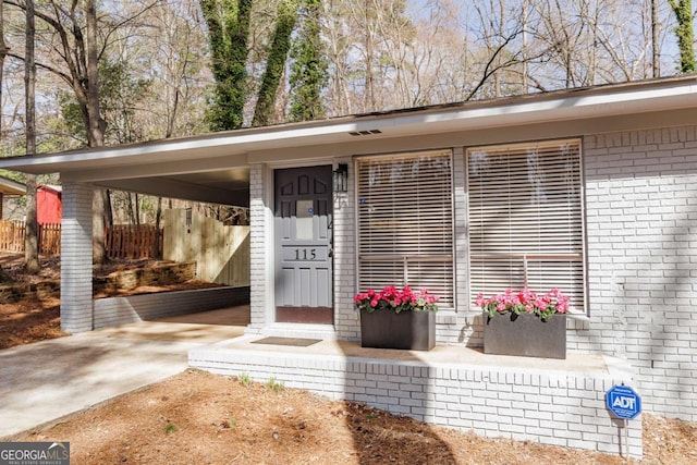 doorway to property featuring a carport, brick siding, driveway, and fence