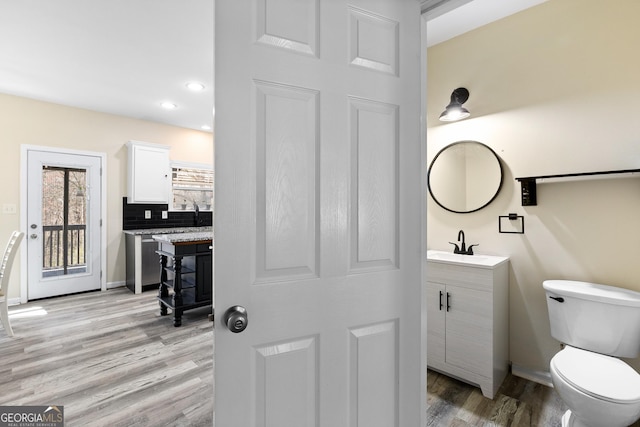 bathroom with vanity, wood finished floors, baseboards, toilet, and tasteful backsplash