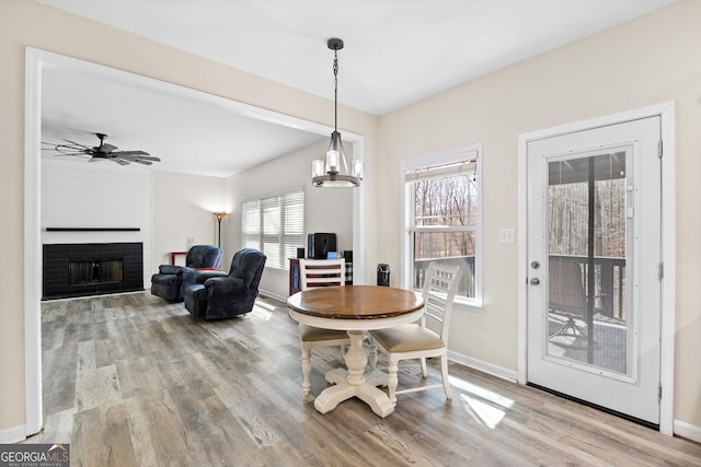 dining room with a fireplace, a ceiling fan, baseboards, and wood finished floors