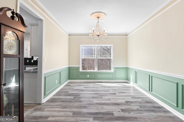 unfurnished dining area with crown molding, a notable chandelier, wood finished floors, and wainscoting