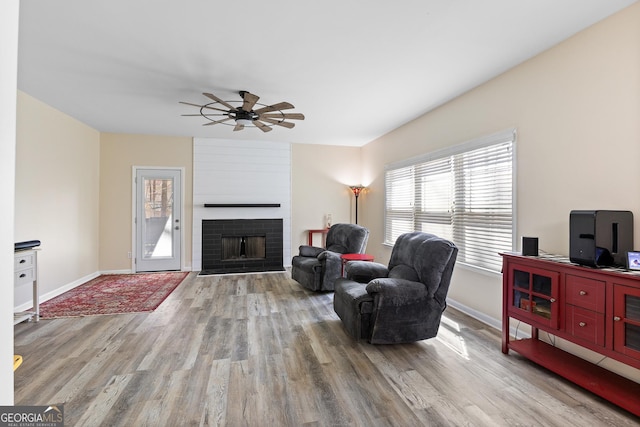 living area featuring baseboards, a brick fireplace, and wood finished floors