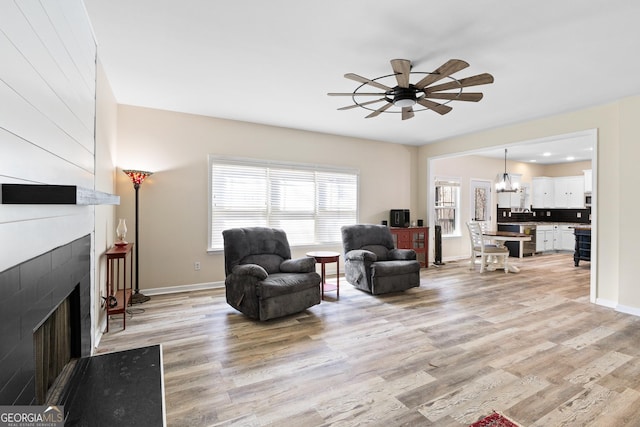 living room with ceiling fan with notable chandelier, a fireplace, light wood-type flooring, and baseboards