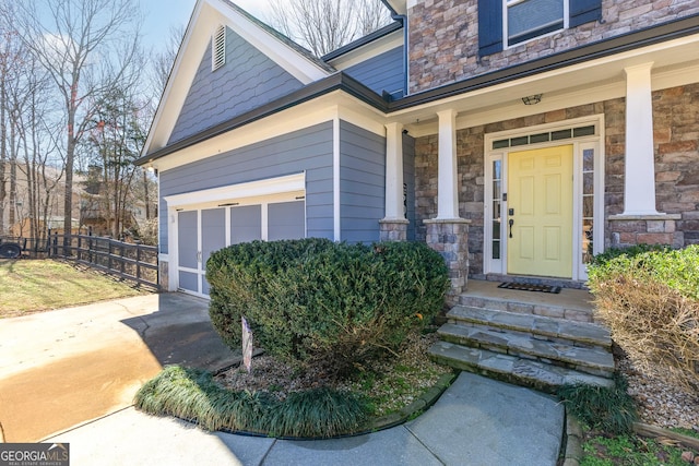 entrance to property with stone siding, a porch, fence, concrete driveway, and a garage