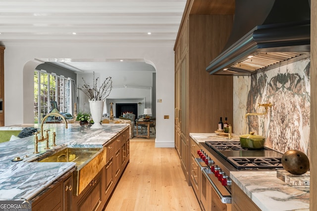 41 Blackland Rd NW, Atlanta, GA 30342 - kitchen with arched walkways, light wood-type flooring, custom exhaust hood, brown cabinetry, and a lit fireplace