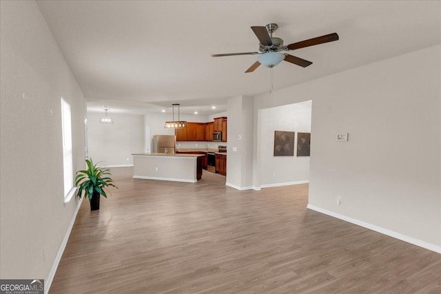 unfurnished living room with light wood-type flooring, baseboards, and ceiling fan with notable chandelier