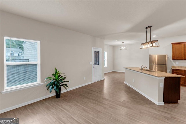 kitchen with light wood-type flooring, baseboards, a center island with sink, and freestanding refrigerator