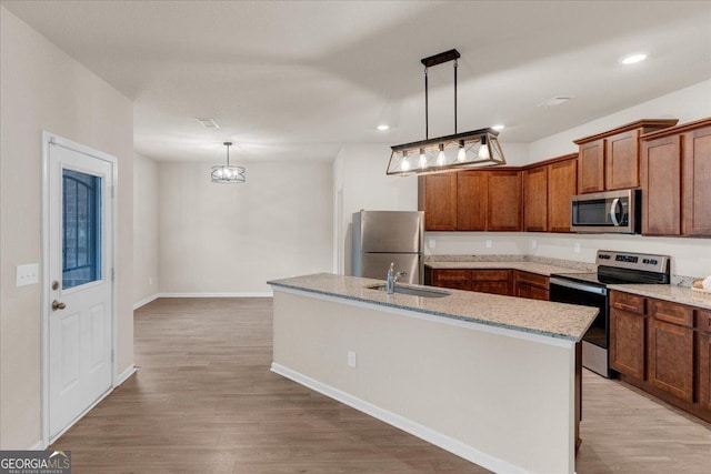 kitchen featuring light stone countertops, an island with sink, appliances with stainless steel finishes, light wood-style floors, and a sink