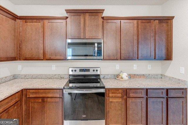 kitchen with light stone countertops, appliances with stainless steel finishes, and brown cabinets