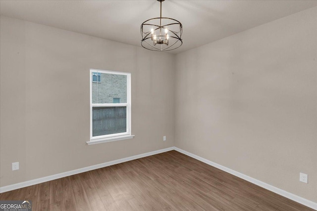 empty room featuring a notable chandelier, baseboards, and wood finished floors