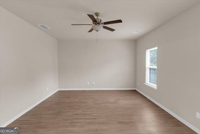 empty room featuring a ceiling fan, wood finished floors, visible vents, and baseboards