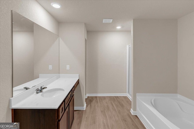 bathroom featuring a garden tub, wood finished floors, recessed lighting, baseboards, and vanity