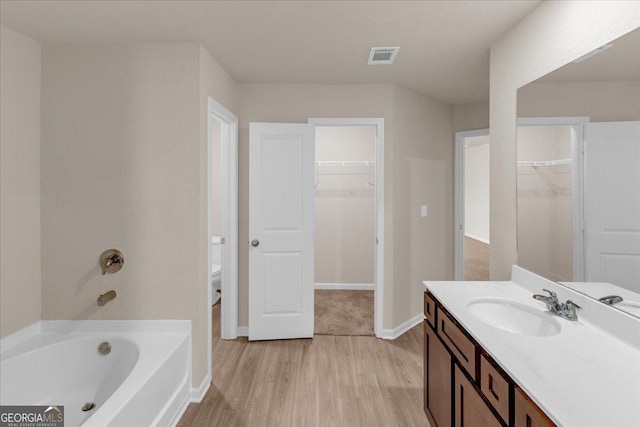 bathroom featuring vanity, wood finished floors, visible vents, a tub to relax in, and toilet