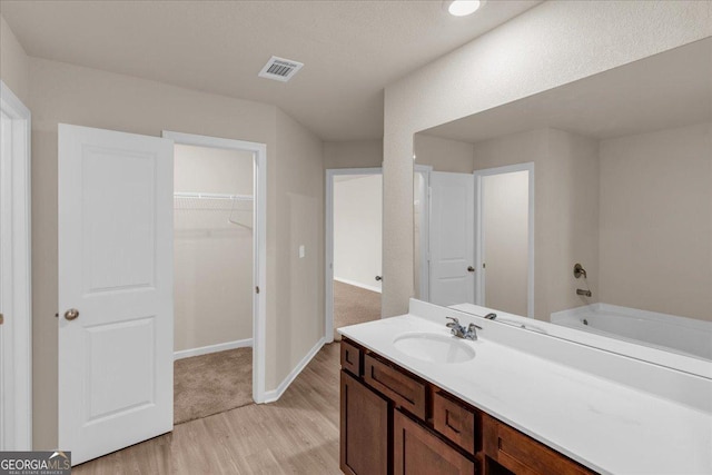 bathroom with visible vents, wood finished floors, vanity, baseboards, and a spacious closet