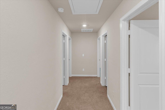 hallway featuring attic access, baseboards, visible vents, and light carpet