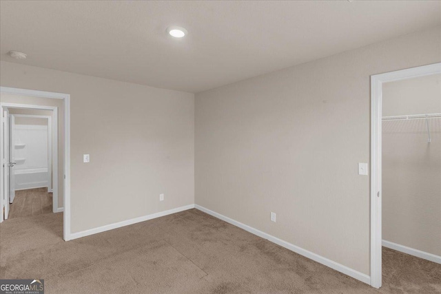 unfurnished bedroom featuring a closet, a walk in closet, baseboards, and carpet floors