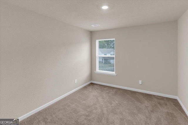 carpeted spare room with visible vents, baseboards, and a textured ceiling