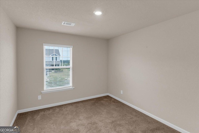 carpeted empty room featuring baseboards, visible vents, and a textured ceiling