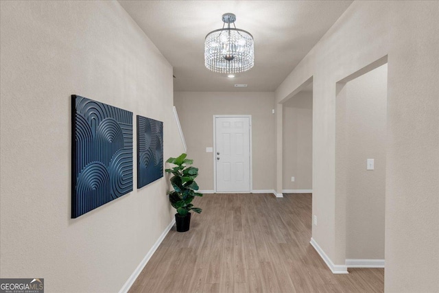 hallway with baseboards, an inviting chandelier, and wood finished floors