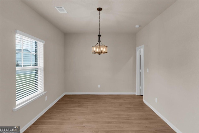 unfurnished dining area featuring a notable chandelier, visible vents, light wood-style flooring, and baseboards