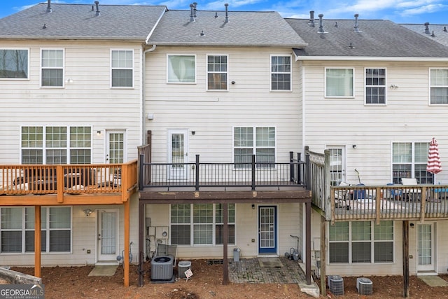 back of property with a deck, cooling unit, and roof with shingles