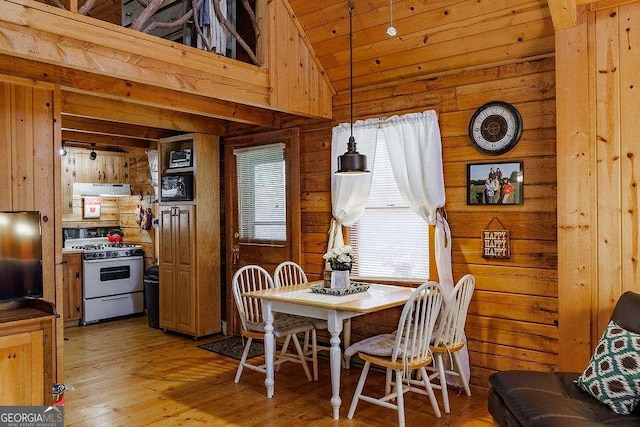 dining room featuring light wood-type flooring, wood walls, and vaulted ceiling