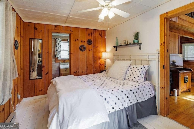 bedroom with light wood-style flooring, wood walls, and ceiling fan