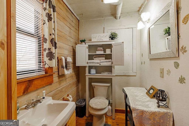 half bathroom with a sink, toilet, wood finished floors, and wooden walls